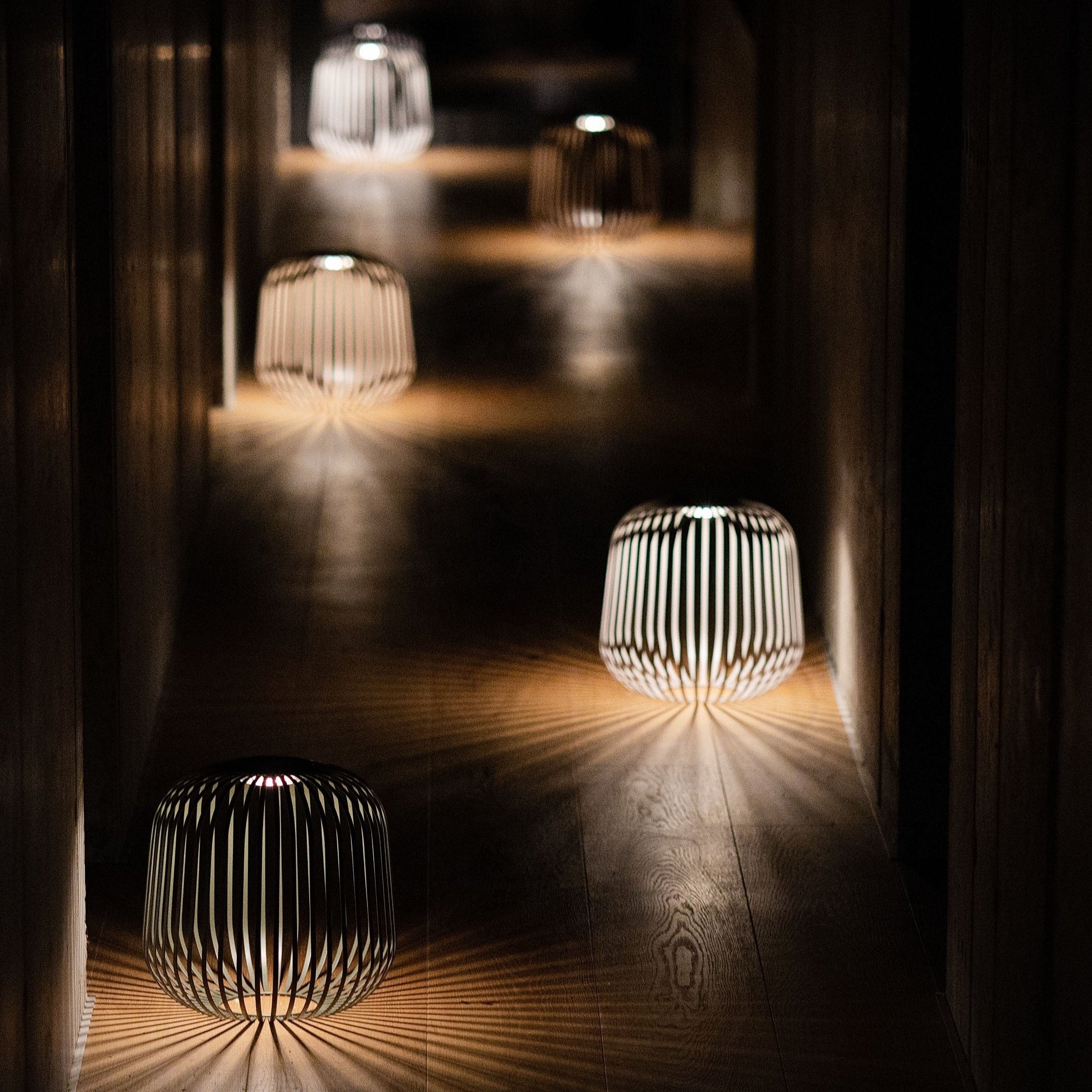 Mehrere Solis Solarlaternen von LUUK Studio spenden stimmungsvolles Licht im dunklen Flur – atmosphärische Nachtbeleuchtung mit dekorativem Schattenspiel.