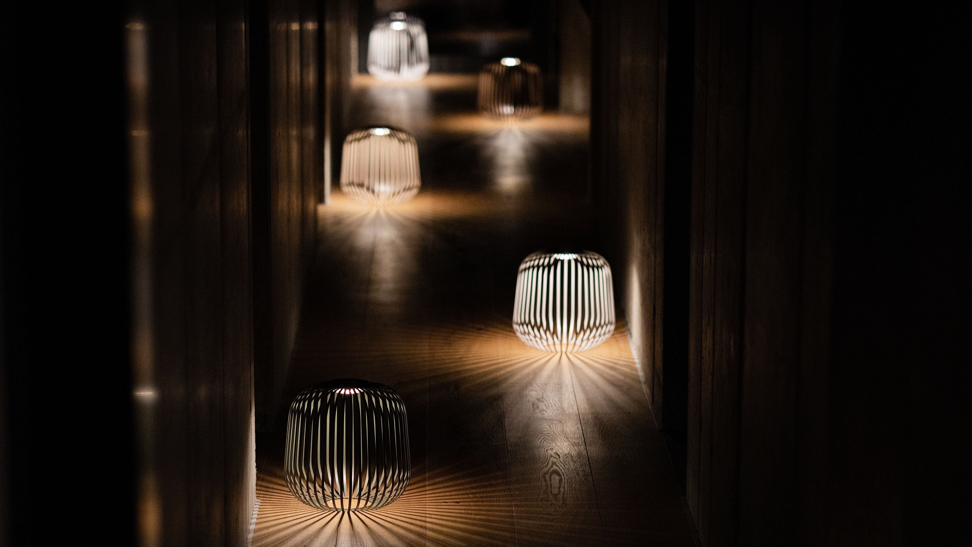 Mehrere Solis Solarlaternen von LUUK Studio spenden stimmungsvolles Licht im dunklen Flur – atmosphärische Nachtbeleuchtung mit dekorativem Schattenspiel.