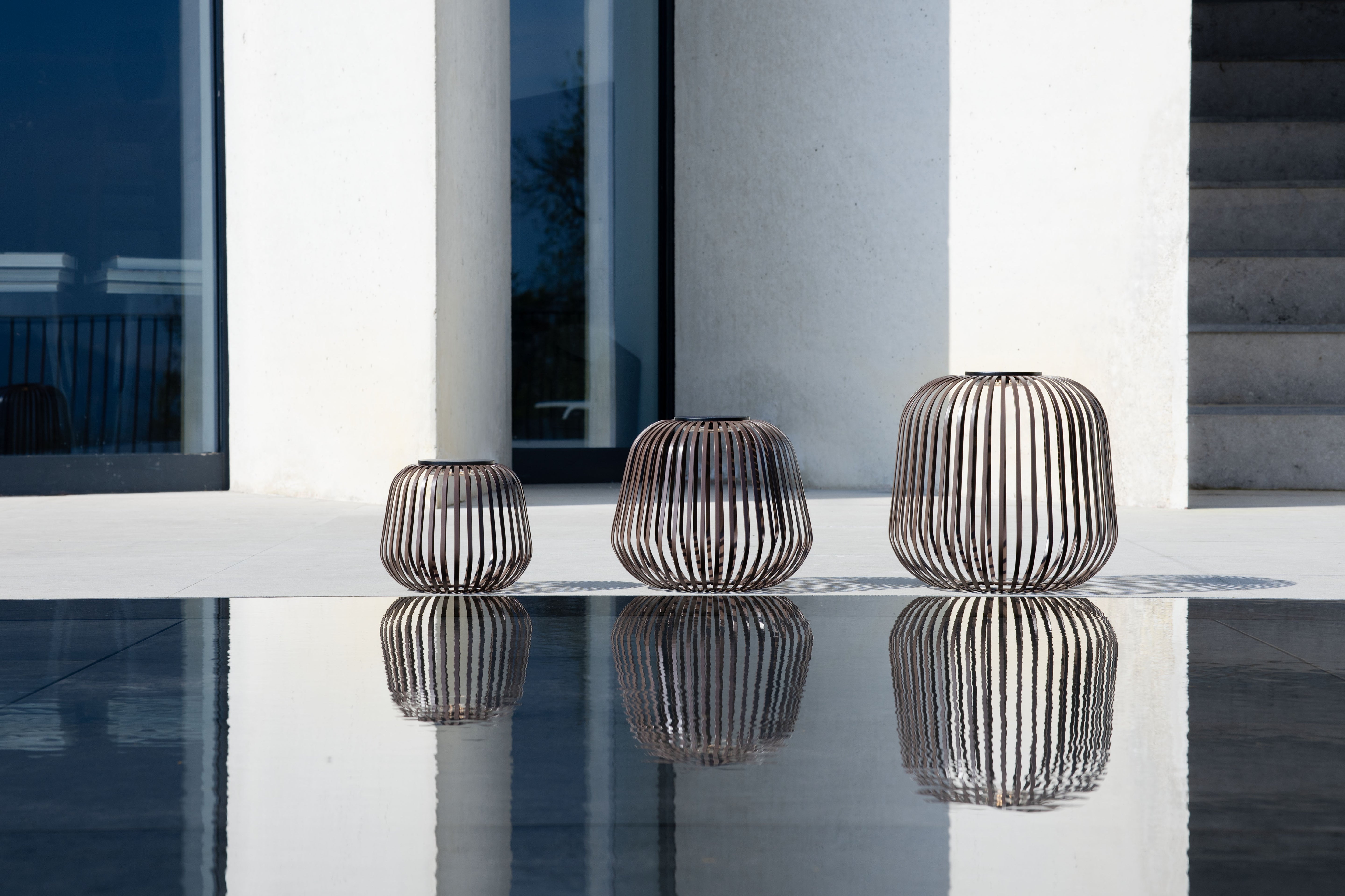 Drei braune Solis Solarlaternen von LUUK Studio auf heller Terrasse – modernes Outdoor-Design mit eleganter Lichtwirkung