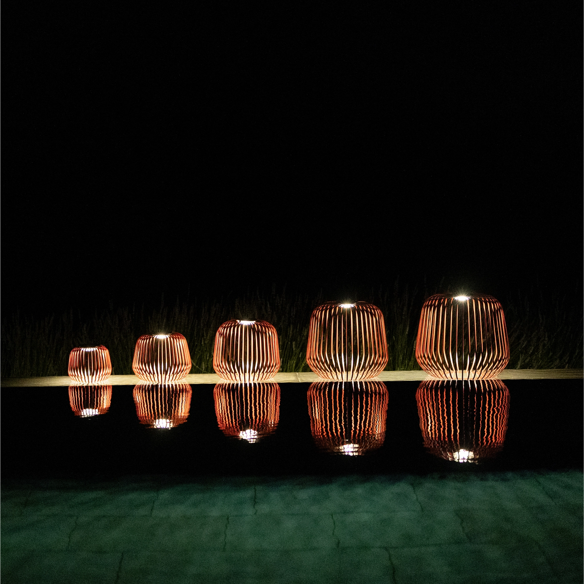 5er Set SOLIS Solarleuchte von LUUK Studio in den Größen S, M, L, XL, XXL in Schwarzkirsche bei Nacht mit Spiegelung im Wasser